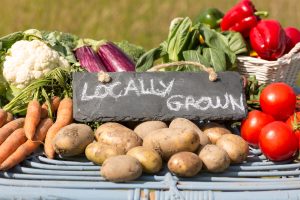 Slate Sign Reading 'locally Grown' Among Fresh Vegetables Like Carrots, Potatoes, Tomatoes, Peppers, and Greens.