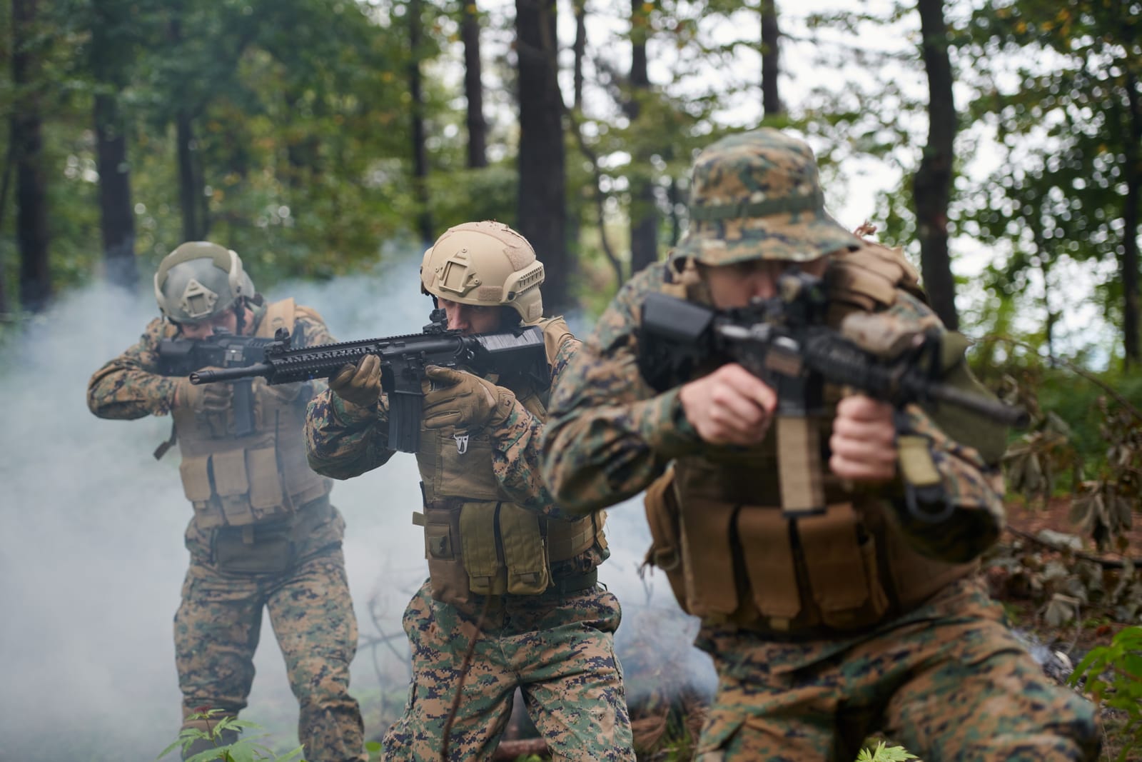 Three Soldiers in Camouflage Gear Fire Rifles in a Smoky Forest During Training.